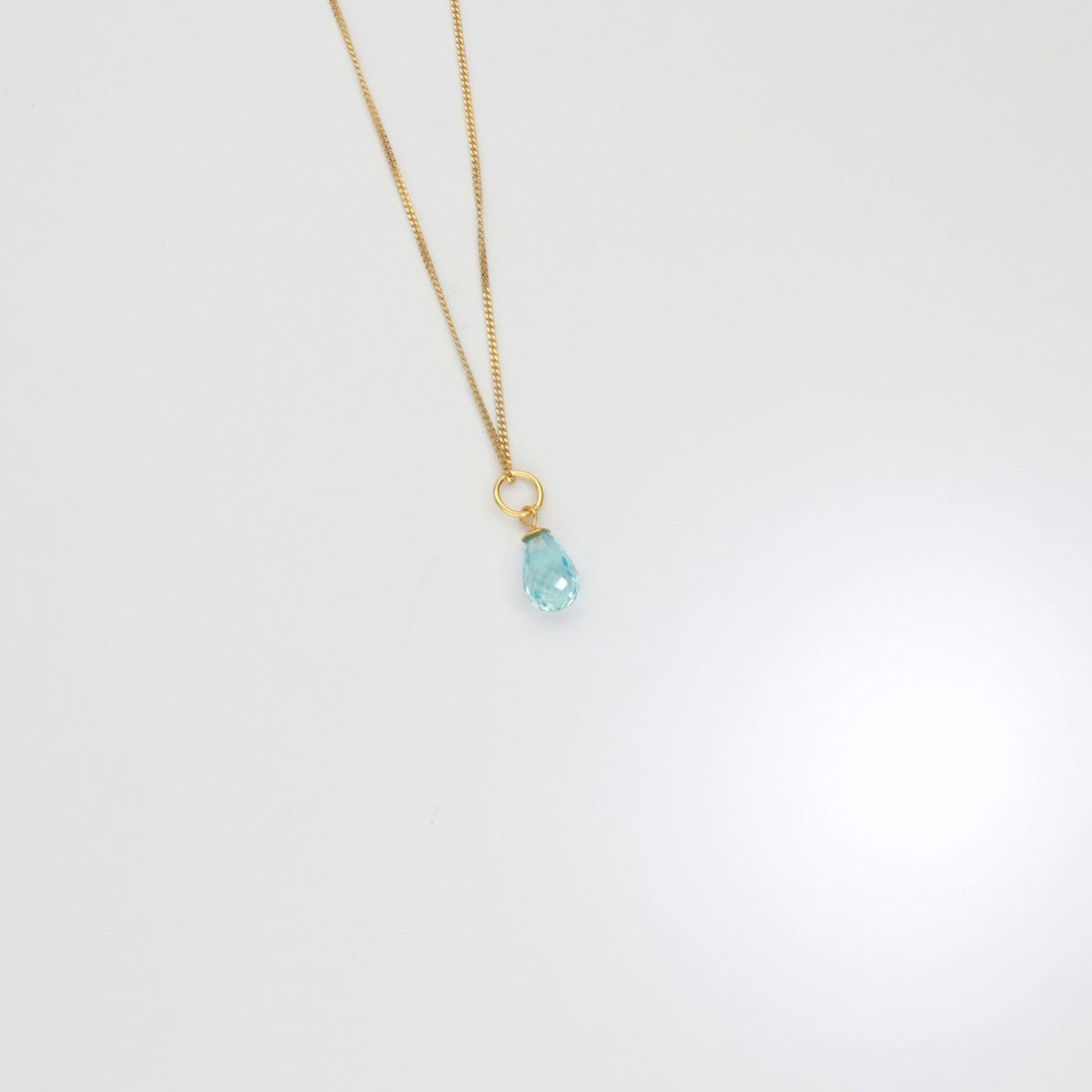 Gold necklace with a blue pendant on a white background