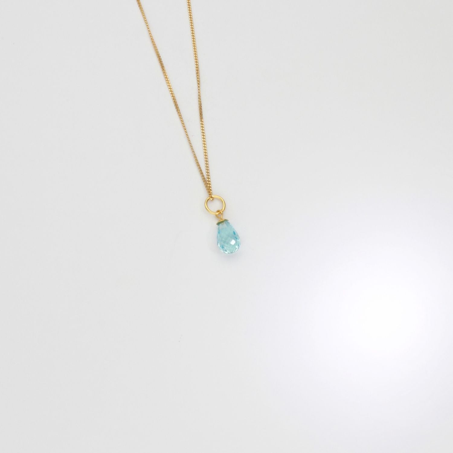 Gold necklace with a blue pendant on a white background