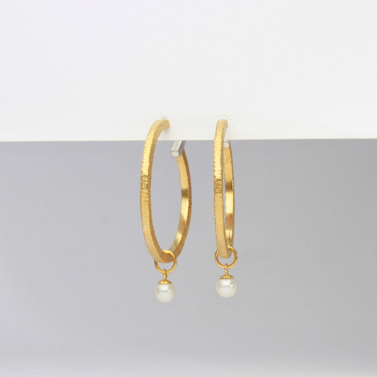 Gold hoop earrings with pearl drops on a gray background