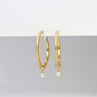 Gold hoop earrings with pearl drops on a gray background