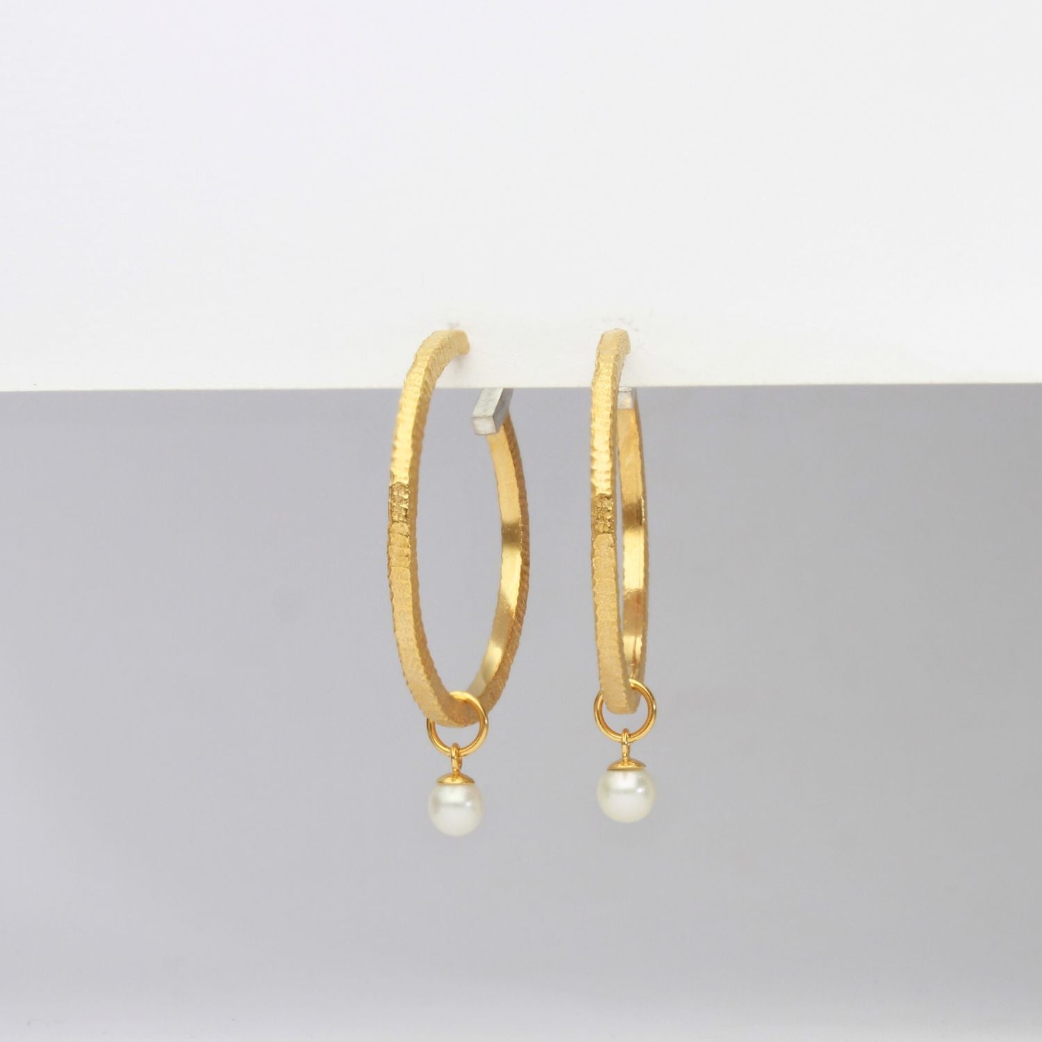 Gold hoop earrings with pearl drops on a gray background