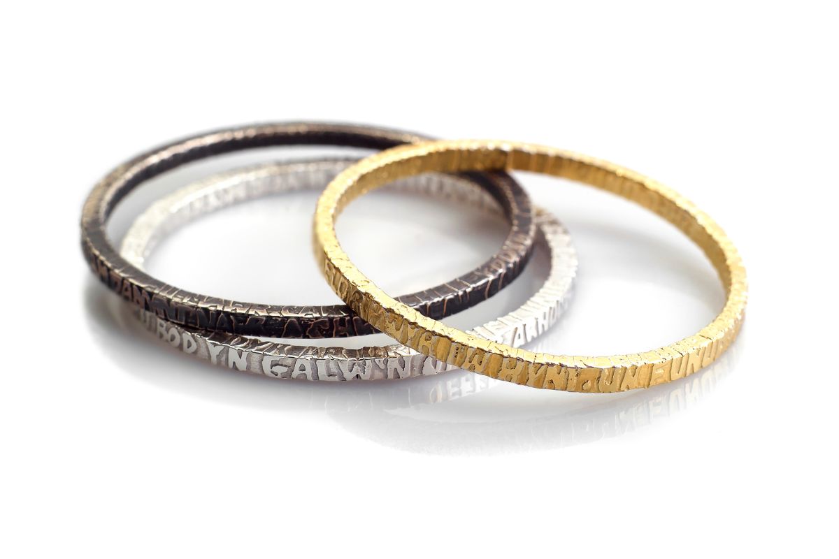 Silver gold and black silver bangles etched with the poem cofio (Remember) by Welsh poet Waldo Williams