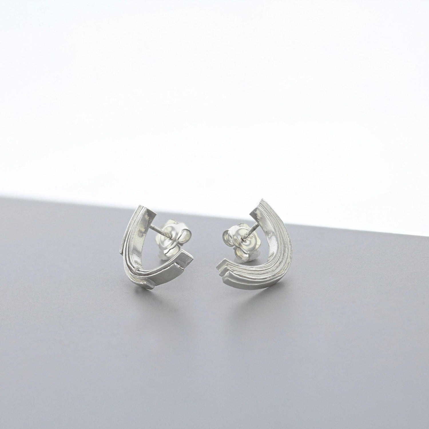 Brushstroke silver half-curve earring, close-up of the fluid line