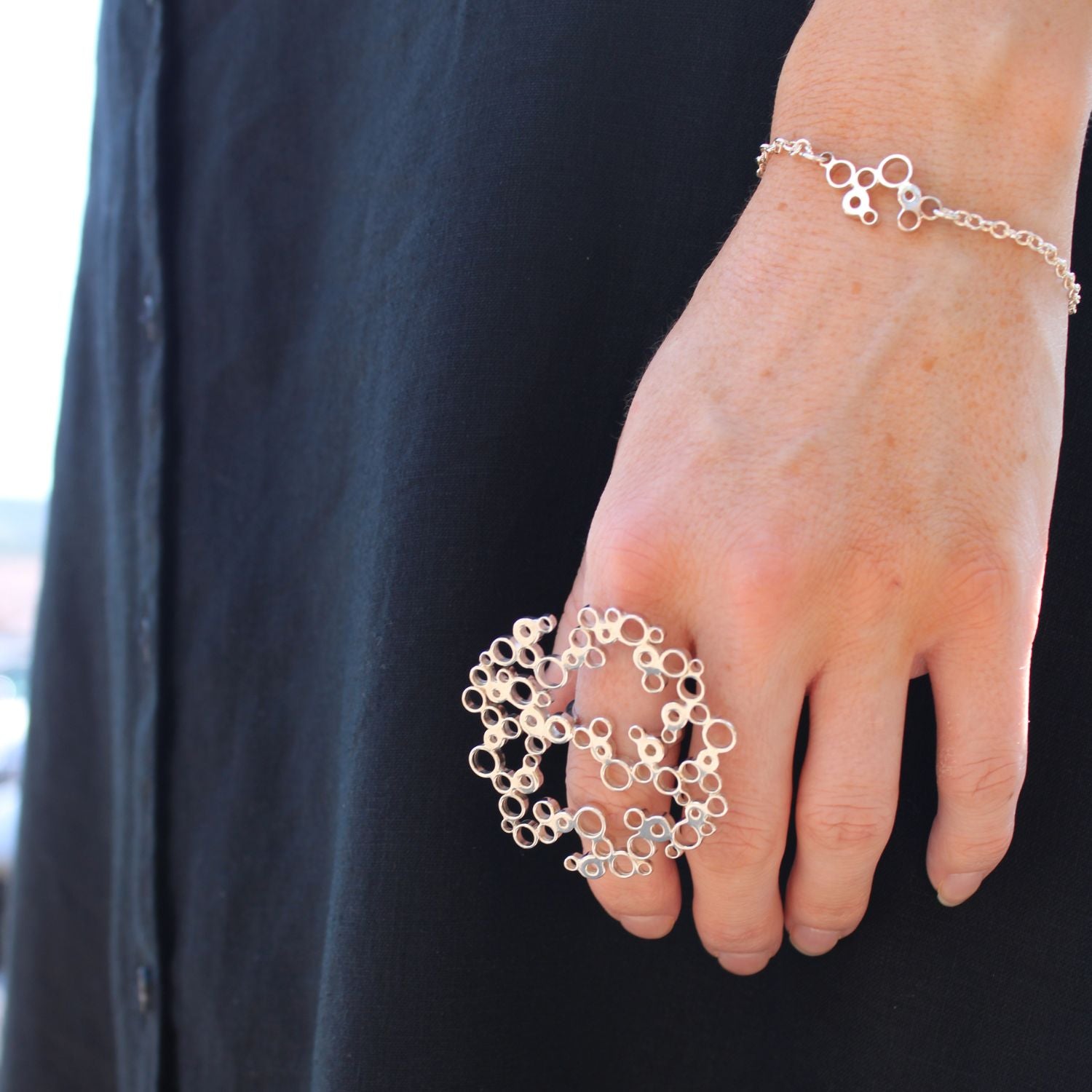 Model wearing the Bubbles large ring alongside the charm bracelet, effervescent design — Modrwy Arian