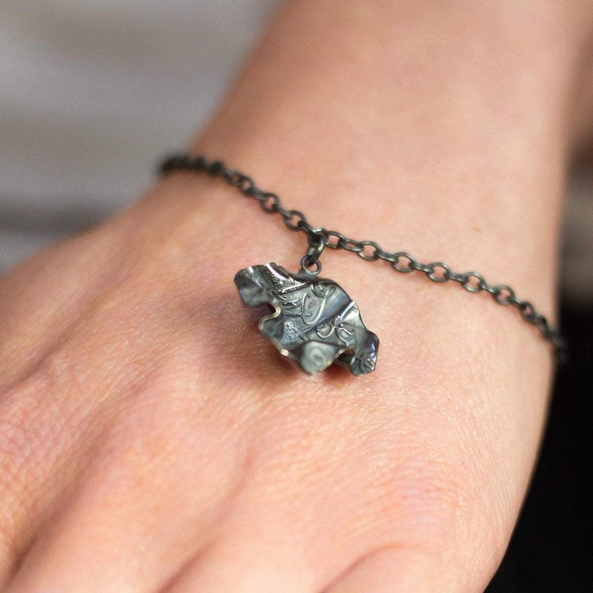 Close-up of the Decorative Concepts black silver charm, echoing a writer's pencil line — Breichled Arian
