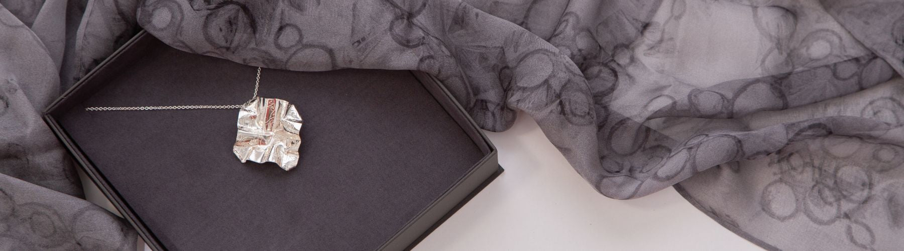 Silver necklace with a large square pendant on a dark surface with gray fabric in the background